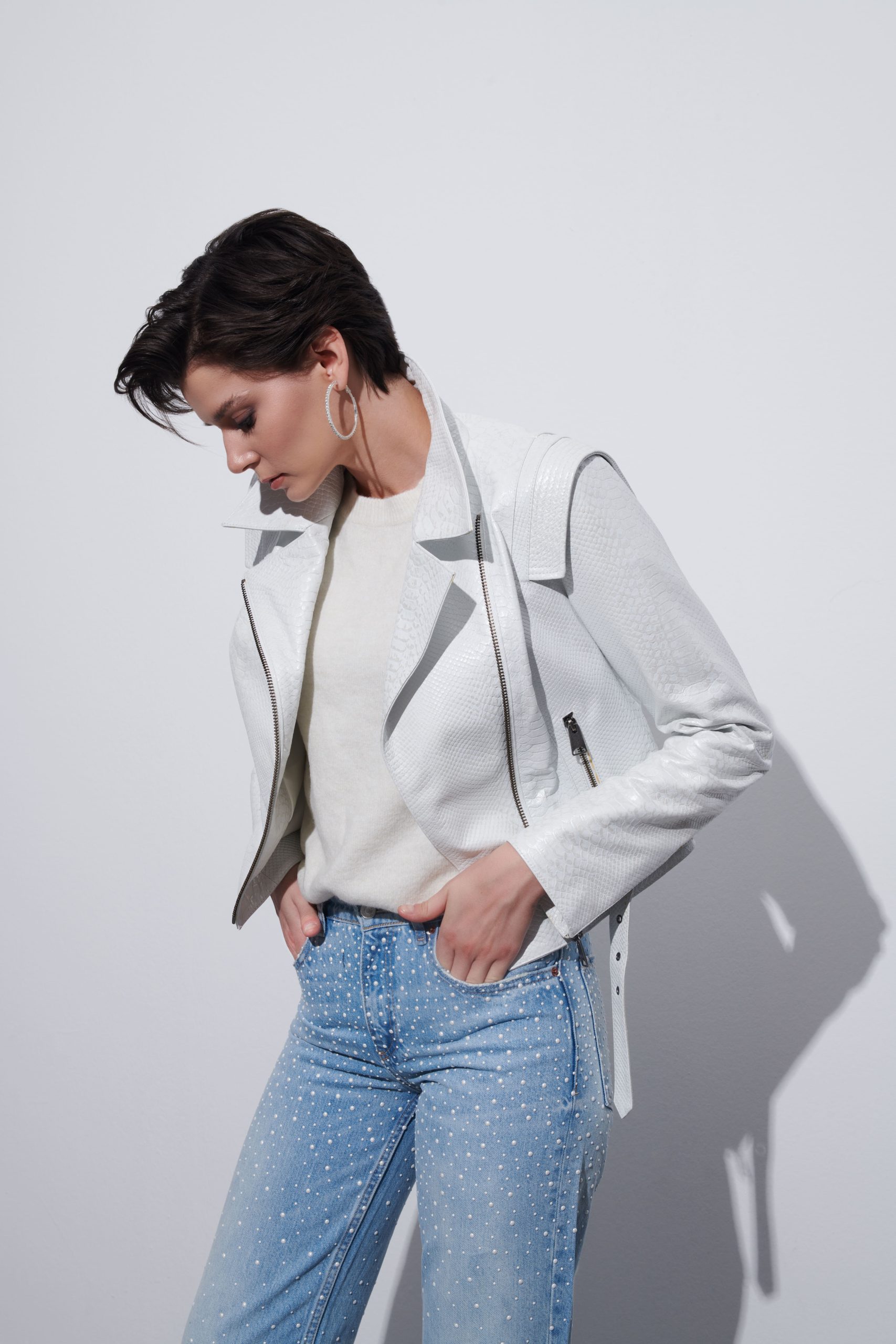 A woman in a white leather jacket with blue jeans.