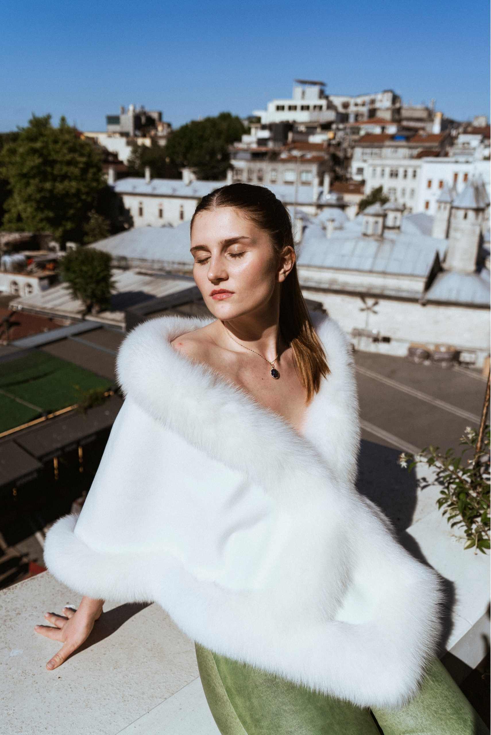 Model wearing a white fur coat with the Istanbul skyline in the background, representing Turkish luxury fashion and craftsmanship.